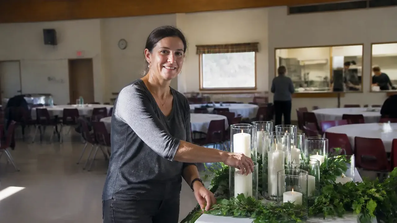Staff member arranging unlit candles in a sunlit sanctuary aisle