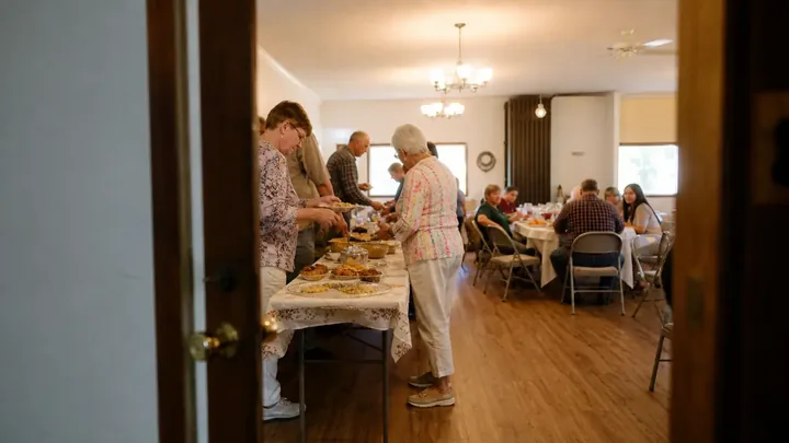 View through a doorway of people serving food and sitting at tables in a hall