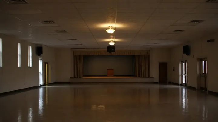 Empty sanctuary showing wooden pews and stacked chairs under one light